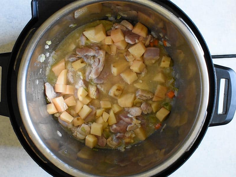 overhead shot of instant pot with chicken stock now added along with half cooked chicken and chunks of white potatoes.