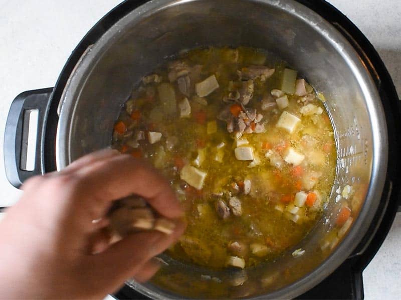 a hand is dropping small squares of biscuit dough into a soup of chicken stock, potatoes, chicken and veggies for instant pot chicken and dumplings.
