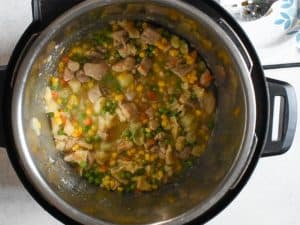 frozen corn and frozen peas sit atop of chicken and dumplings in an instant pot. There is a large slotted spoon sitting on a plate in the upper right corner.