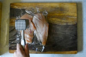 chicken breasts being beaten with a metal meat mallet