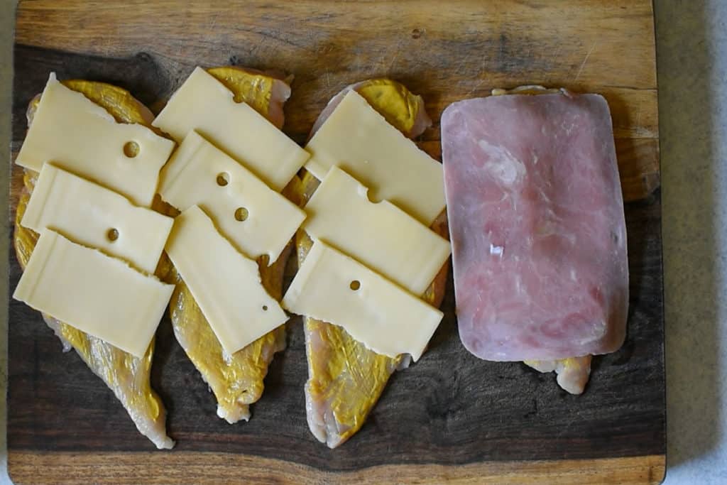 chicken breast cut with mustard, swiss cheese and ham on a wooden cutting board.