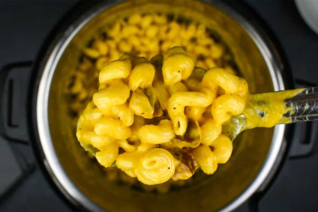 a serving spoon holding up macaroni and cheese above an instant pot